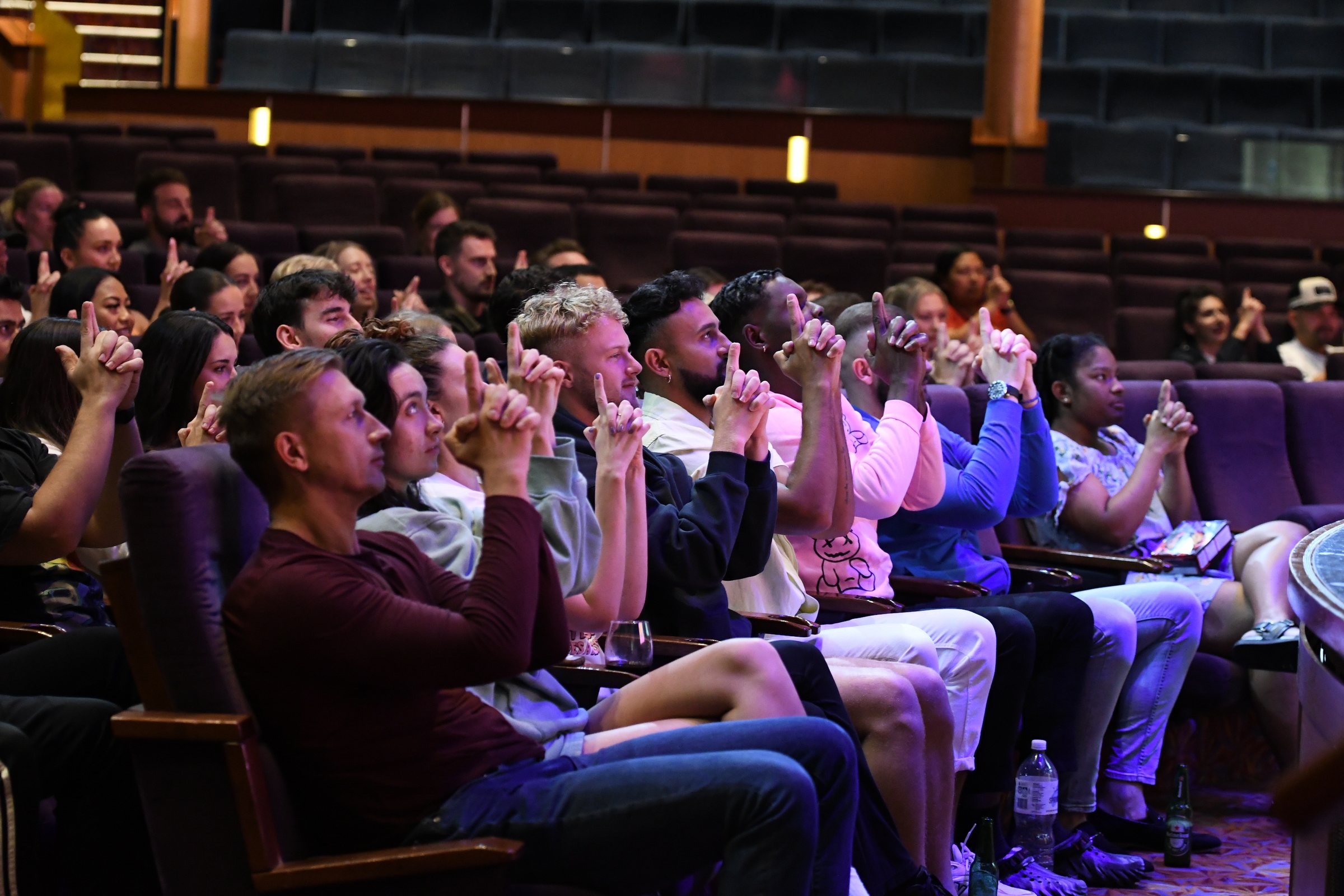 A theatre audience mid-laugh, hands over their faces, watching the comedy hypnosis show