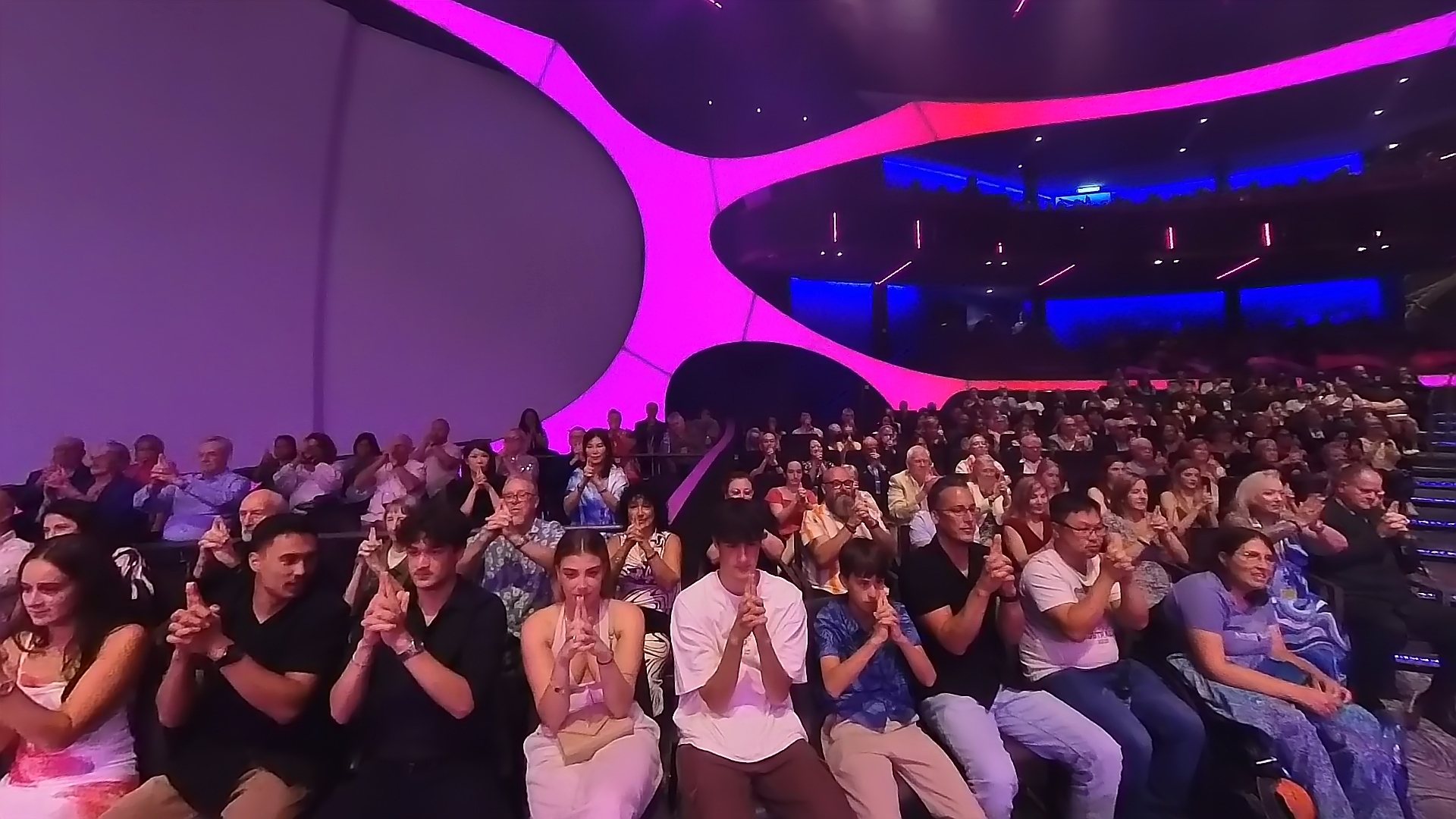 Wide view of a full theatre audience with hands clasped during the hypnosis routine