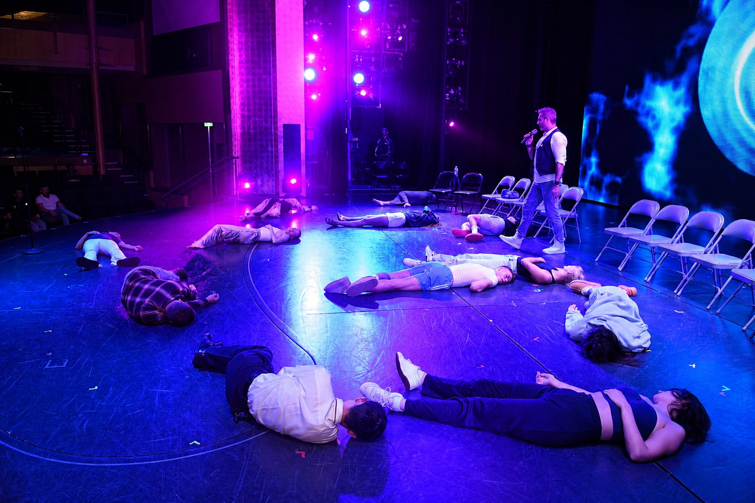 Hypnotised volunteers lying across a cruise theatre stage under blue light